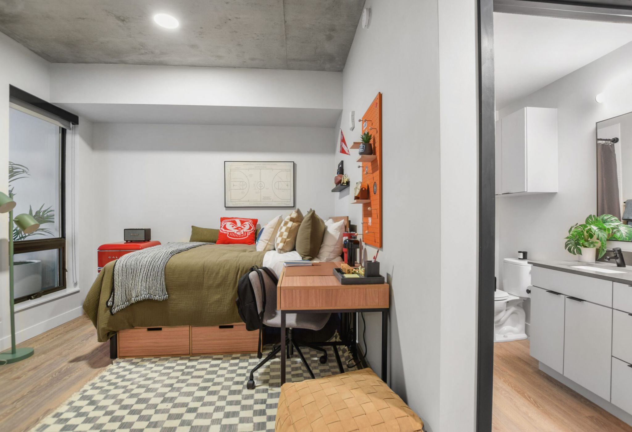 Modern, neatly organized bedroom with a bed, desk, chair, and visible bathroom. Warm tones and natural light.