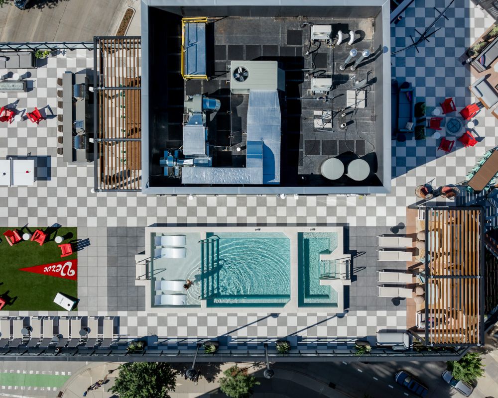 Aerial view of a rooftop with a pool, seating areas, and checkerboard flooring.