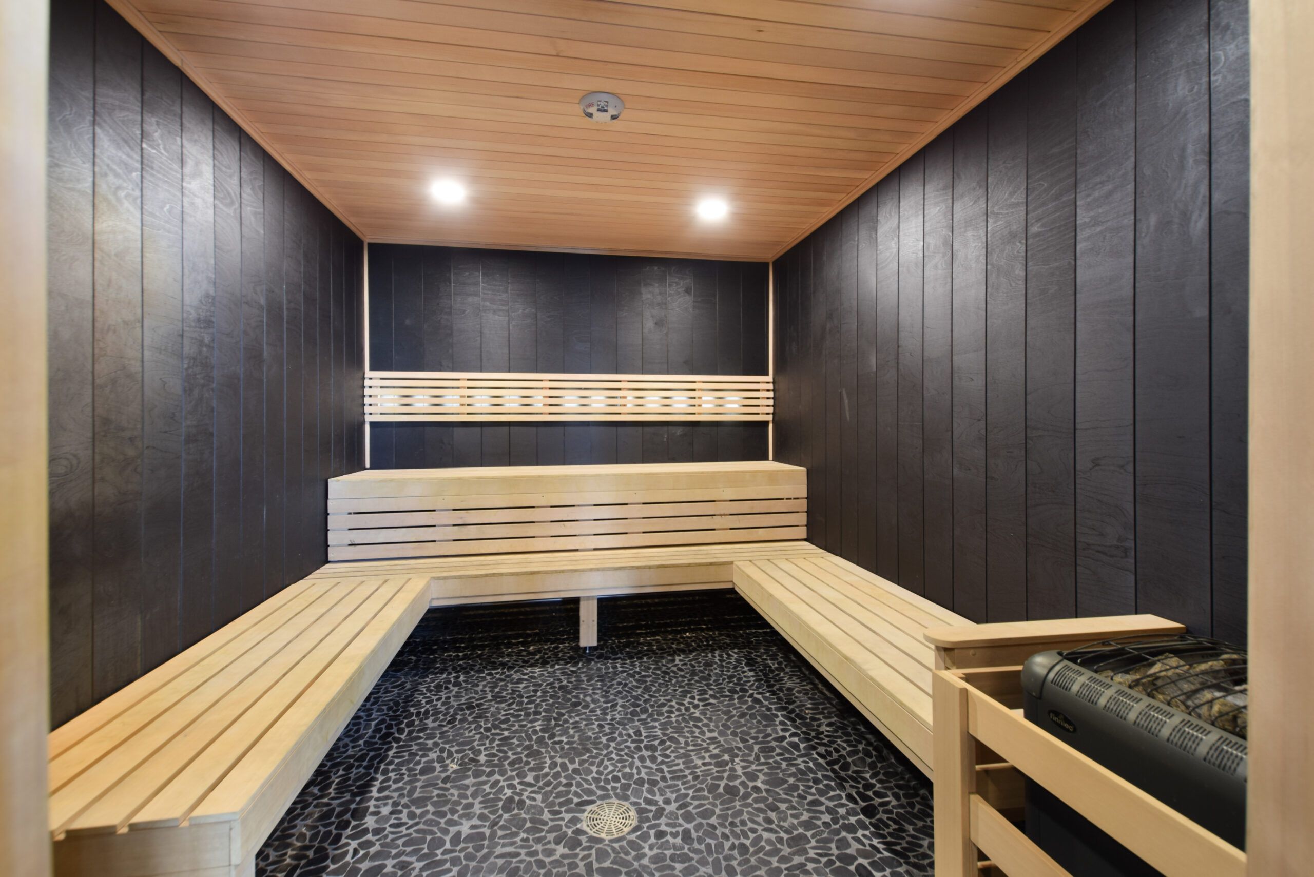 Modern sauna interior with wooden benches and dark walls, illuminated by ceiling lights.