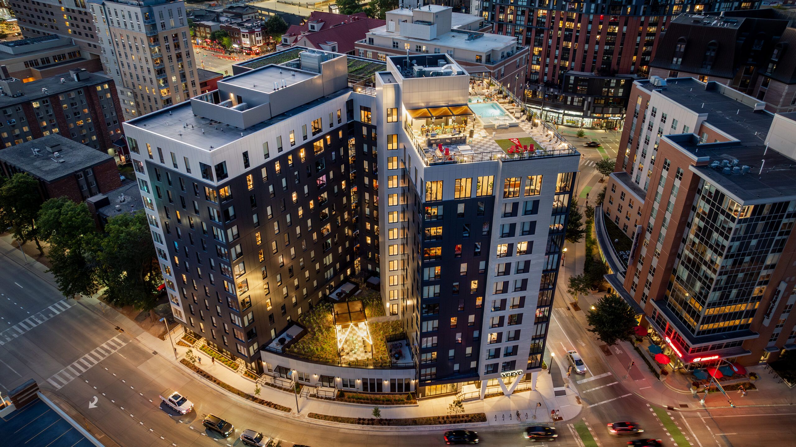 Aerial view of a modern city building with rooftop amenities and surrounding urban area at dusk.