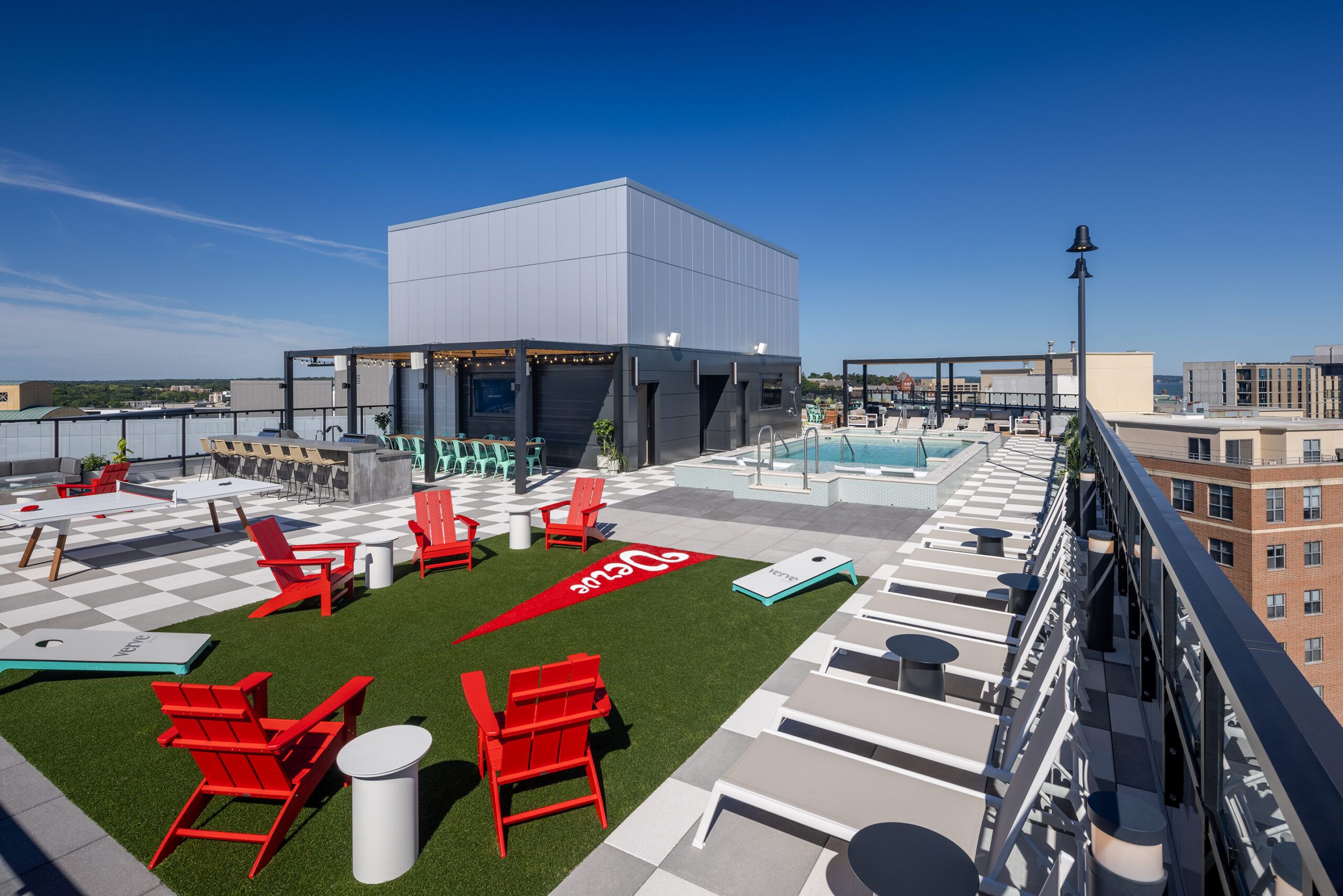 Rooftop with chairs, tables, a pool, and lawn games under a clear blue sky.