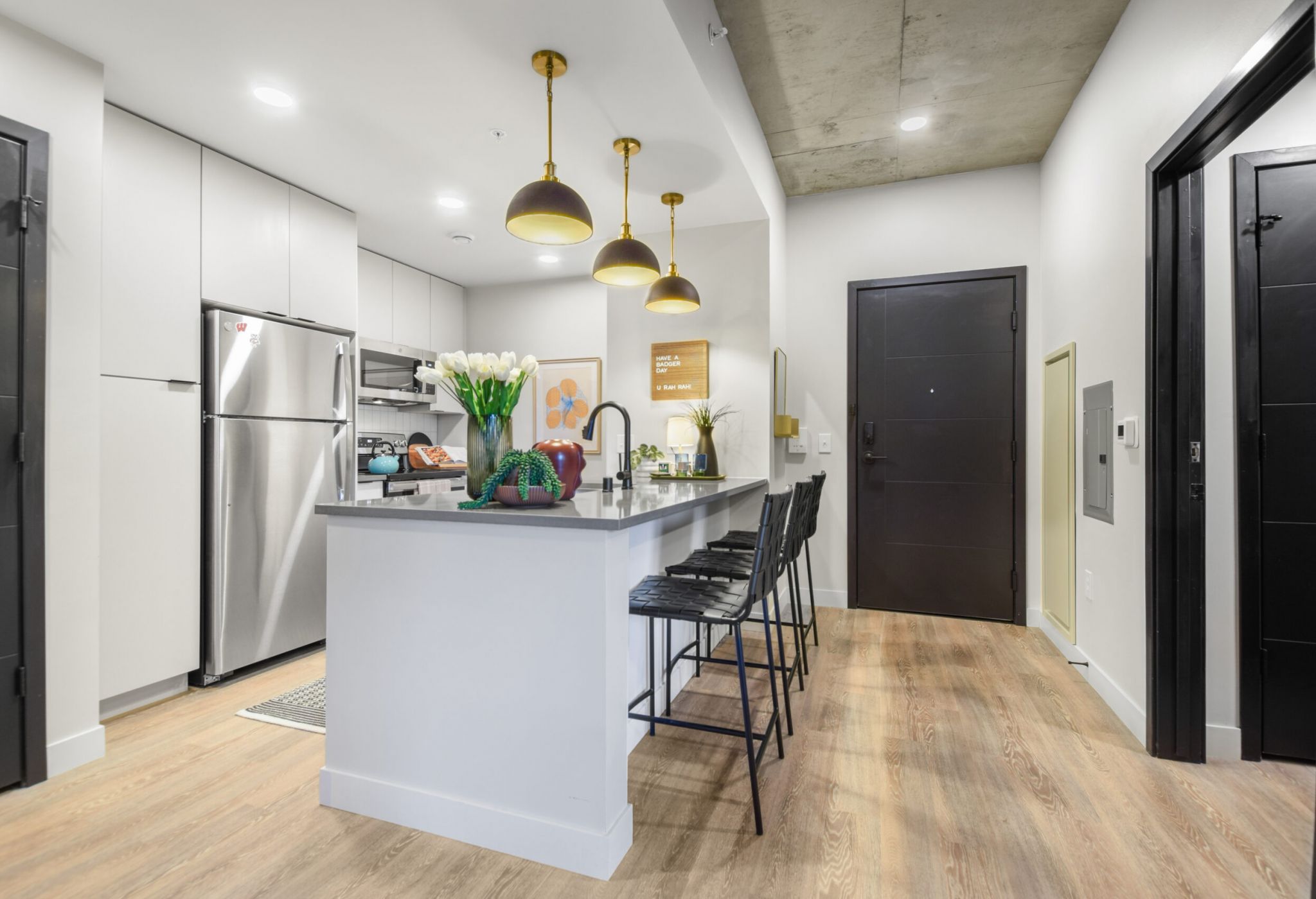 Modern kitchen with island, bar stools, and pendant lights. Stainless steel appliances and wooden flooring.