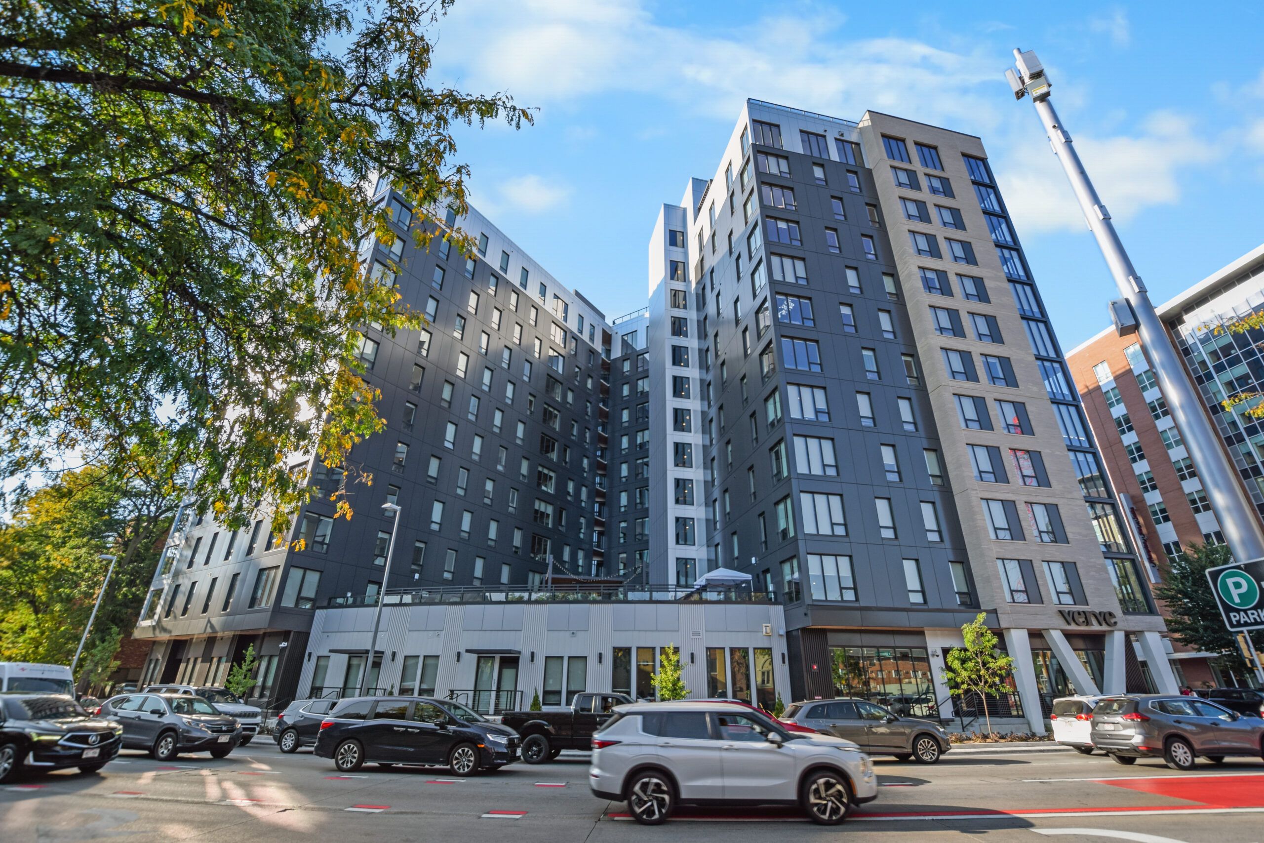 A modern, multi-story apartment building with cars parked on the street in daylight.